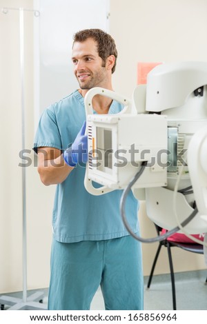 Young male nurse looking away while adjusting xray machine in examination room