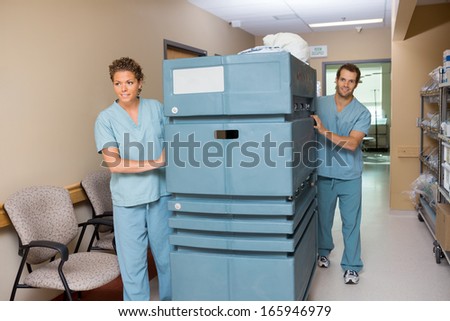 Portrait of male nurse pushing trolley while colleague assisting him in hospital hallway