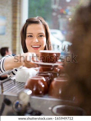 Happy Female Customer Taking Coffee From Waitress In Cafe