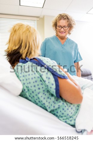 Happy mature female nurse looking at newborn babygirl with mother in hospital