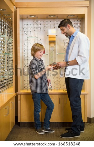 Profile of mid adult male optometrist and boy holding spectacles in store