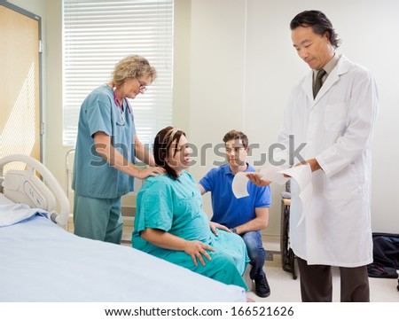 Male doctor examining ctg report with birthing mother, husband and nurse