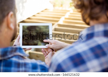 Cropped image of worker pointing at digital tablet while coworker holding it
