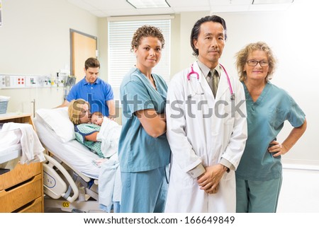 Portrait of successful medical team with newborn baby and parents in background at hospital room