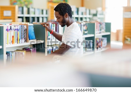Side view of African American male librarian arranging books in bookstore