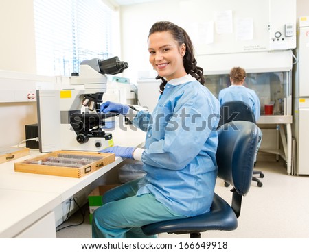 Portrait of happy female researcher with microscope and samples tray working in laboratory