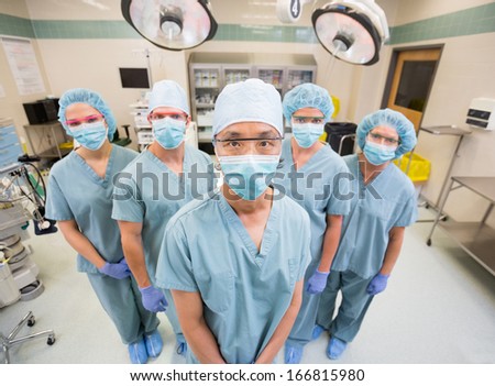 Portrait of confident medical team in scrubs standing inside operation room