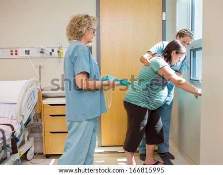 Female nurse carrying hospital gown for pregnant woman while colleague consoling her at window