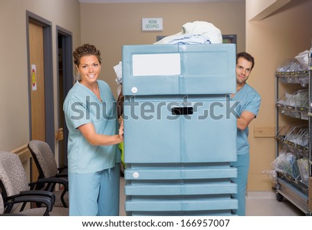 Female and male nurses pushing trolley filled with linen in hospital hallway