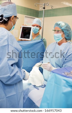 Nurse showing digital tablet to doctor during surgery in operation room