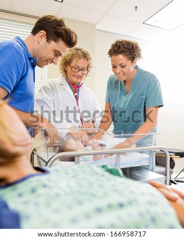 Happy medical team examining newborn babygirl while standing by man with mother in foreground