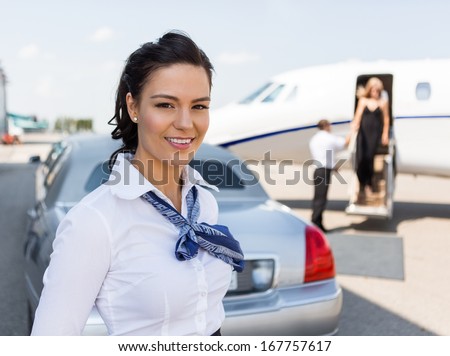 Portrait Of Beautiful Stewardess Standing Against Limousine And Private Jet At Airport Terminal