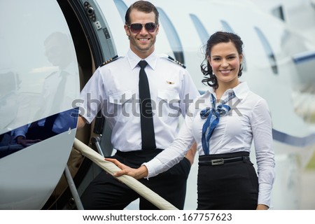 Portrait Of Happy Confident Airhostess And Pilot Standing On Private Jet\'S Ladder