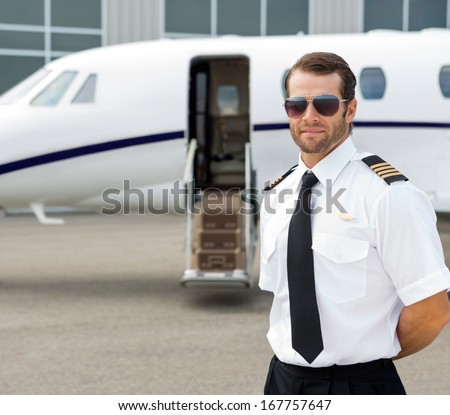 Portrait of confident pilot wearing sunglasses with private jet in background