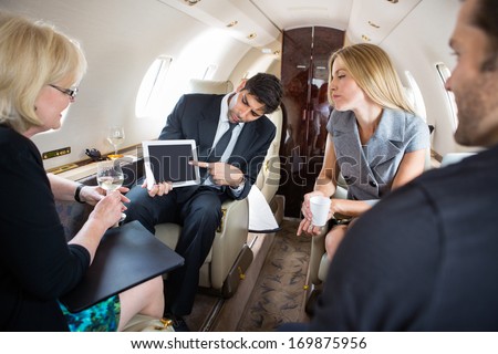 Businessman showing project on digital tablet to partners in private plane