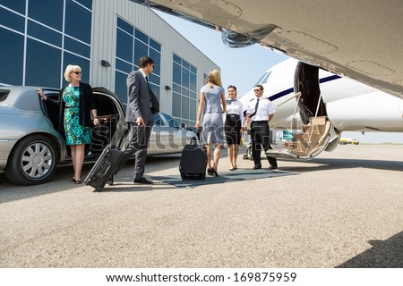 Airhostess and pilot greeting business people before boarding private jet