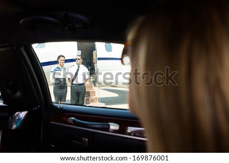 View of airhostess and pilot standing against private jet through limousine window