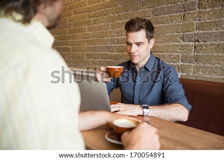 Young man using laptop in cafe while sitting with friend