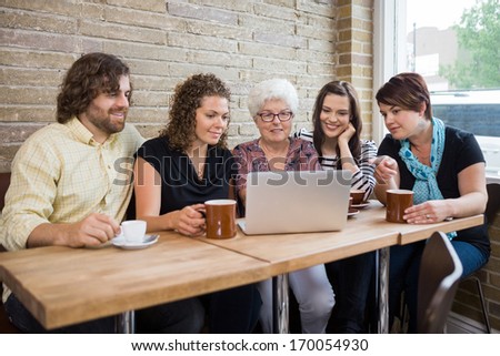Senior Woman With Group Of Friends Using Laptop At Coffeeshop