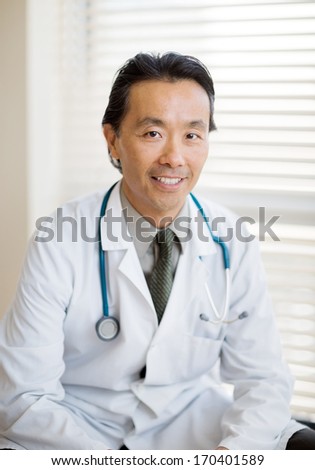 Portrait of Asian male cancer specialist with stethoscope around neck sitting in hospital
