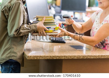 Midsection of schoolboy holding books while librarian scanning them at checkout counter in library