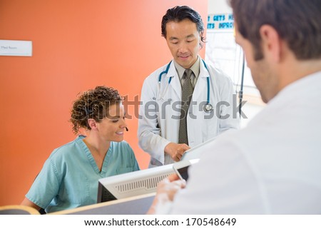Doctor and nurse using digital tablet while patient standing at reception in hospital
