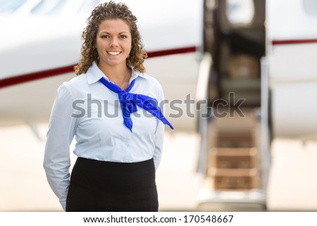 Portrait of beautiful stewardess with private jet in background at terminal
