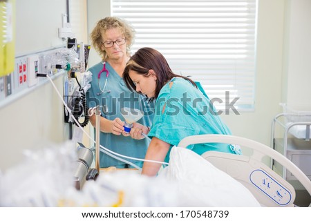 Mature female nurse giving nitrous oxide mask to woman in active labor