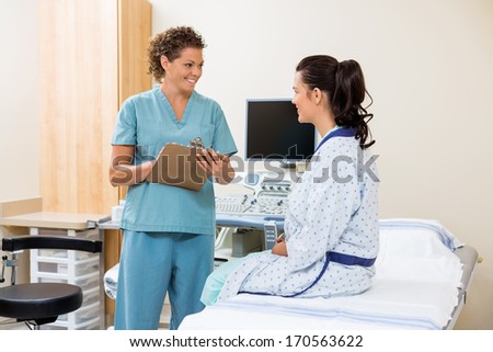 Female Nurse With Clipboard Looking At Patient Before Ultrasound Test In Hospital Room