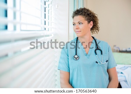 Thoughtful female nurse looking out through window in hospital room