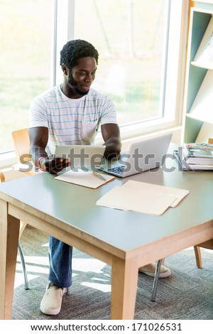 Full length of male university student using digital tablet and laptop while studying in library