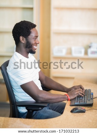 Side view of male librarian working on computer at library desk