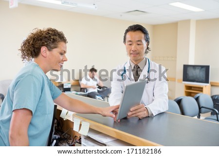 Mature Doctor And Nurse Using Digital Tablet At Hospital Reception