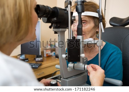 Female optometrist examining senior woman\'s eyes with slit lamp in eye clinic