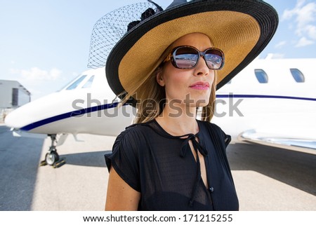 Elegant woman wearing sunglasses and sunhat against private jet