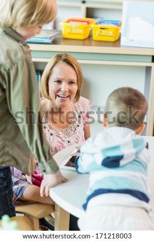 Cheerful mature teacher with children using digital tablet in library