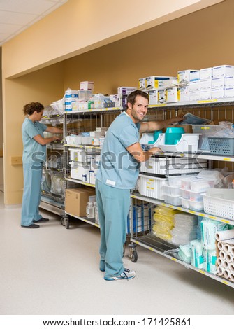 Full length of male and female nurses arranging stock on shelves in hospital storage room