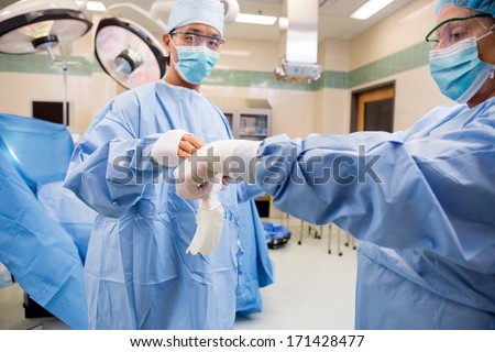 Nurse assisting doctor in putting on surgical glove in operating theater