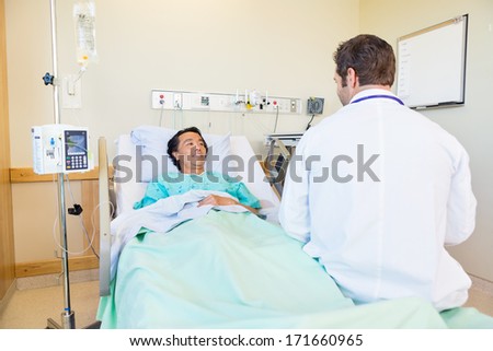 Smiling mature patient looking at doctor while lying on bed in hospital room