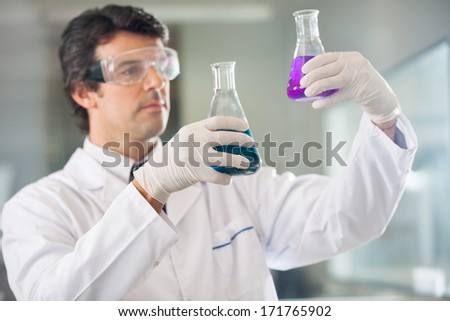 Male scientist examining flasks with different samples in lab