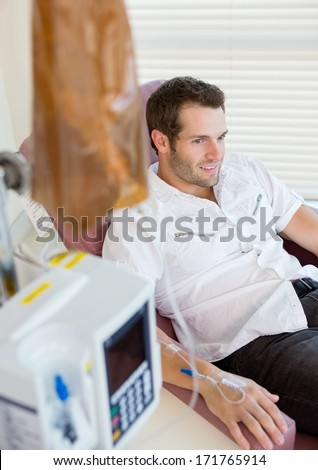 Male patient with IV drip attached to his hand during chemotherapy in hospital room