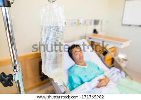 Closeup of IV bag with patient lying in background on hospital bed