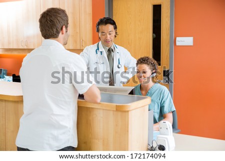 Doctor And Nurse Working At Reception Desk While Man Standing In Hospital