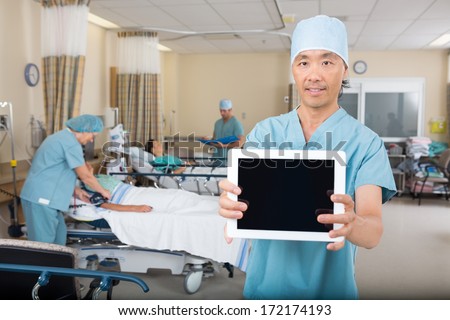 Portrait of mid adult male nurse showing digital tablet in hospital ward
