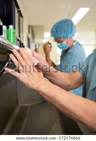 Female surgeon scrubbing hands and arms with colleague before surgery in hospital