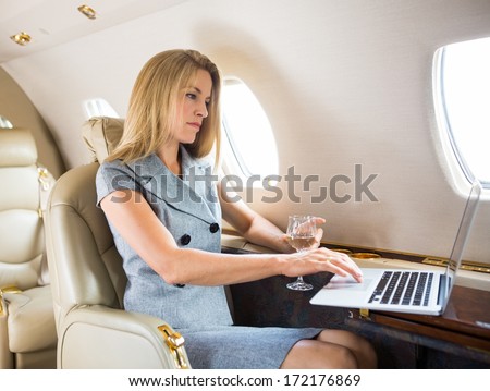 Confident Businesswoman With Wineglass Using Laptop In Private Jet