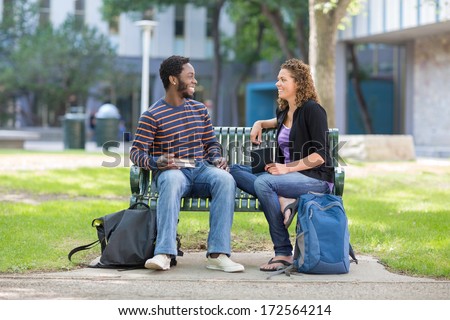 Happy male and female students sitting on bench at university campus