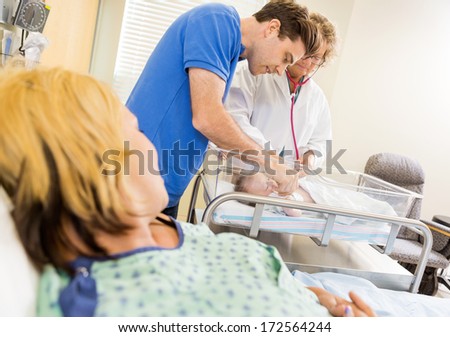 Female mature doctor examining newborn babygirl while mother and father looking at her in hospital