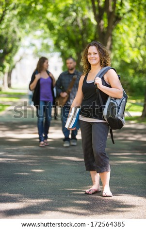 Full length portrait of university student with backpack and book standing on campus road