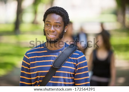 Thoughtful male university student at campus with friends in background
